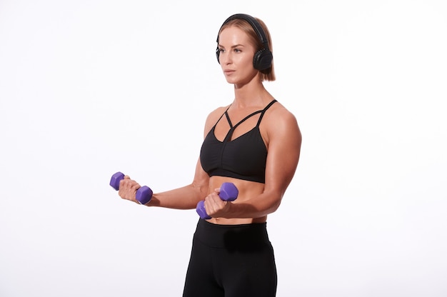 Deportista musculoso fuerte en auriculares y traje negro haciendo ejercicio con pesas sobre fondo blanco aislado