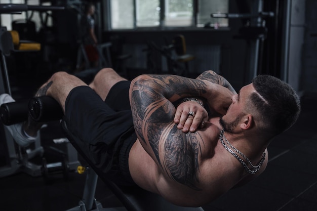 Deportista musculoso tatuado sin camisa haciendo sentadillas en el gimnasio
