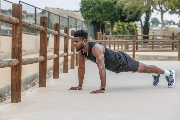 Deportista negro haciendo ejercicio de tabla en el parque