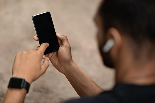 Deportista negro irreconocible usando teléfono celular con pantalla en blanco