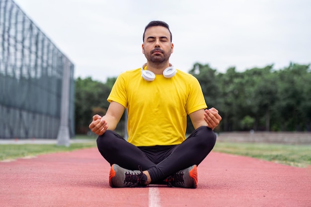 Un deportista pacífico practica la atención plena meditando en la postura del loto en una pista de atletismo de un parque verde