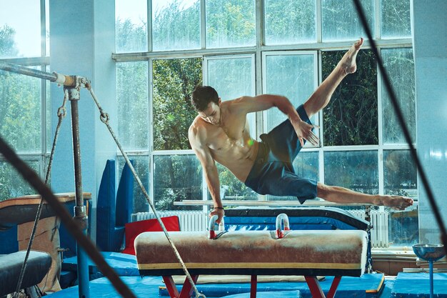 El deportista realizando difícil ejercicio gimnástico en el gimnasio. El deporte, ejercicio, gimnasta, salud, entrenamiento, concepto de atleta. Modelo de ajuste caucásico