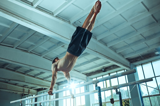 El deportista realizando difícil ejercicio gimnástico en el gimnasio. El deporte, ejercicio, gimnasta, salud, entrenamiento, concepto de atleta. Modelo de ajuste caucásico