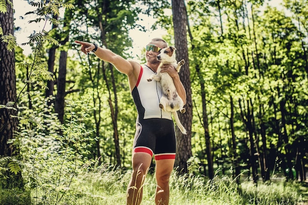 Deportista en ropa deportiva y gafas de sol con su perrito en el bosque verde.