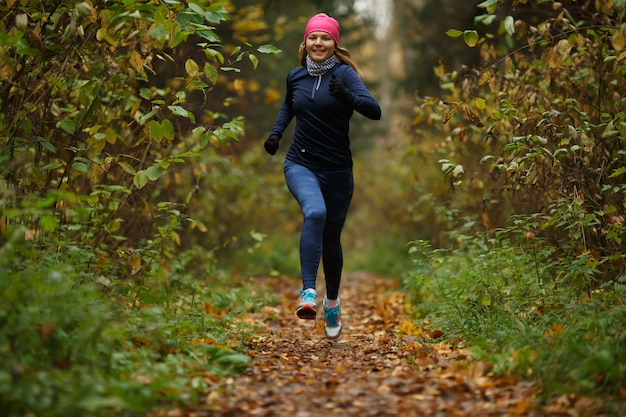 Deportista rubia corre entre árboles en el parque otoño