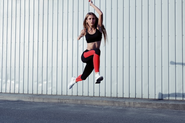 Foto deportista saltando y estirando. longitud total de mujer sana haciendo ejercicio y saltando al aire libre.