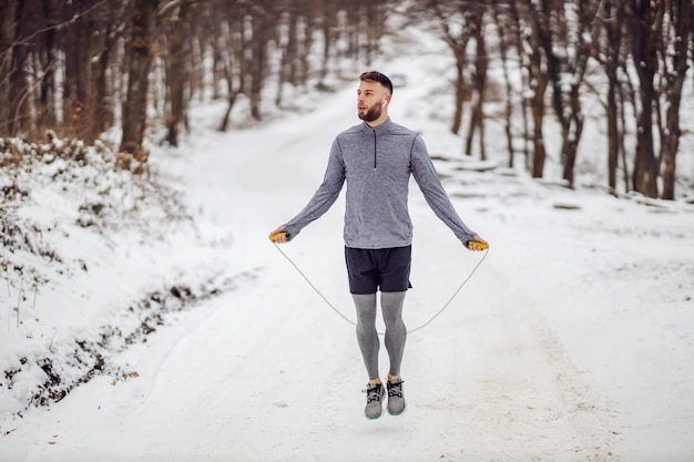 Deportista saltar la cuerda sobre la nieve en invierno en el bosque.