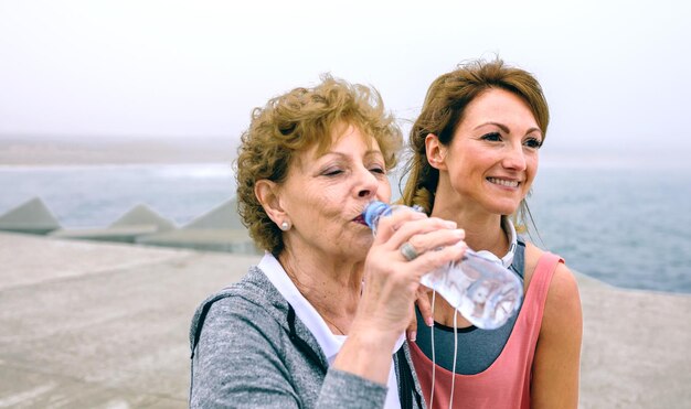 Deportista senior bebiendo agua con entrenadora en el muelle marítimo