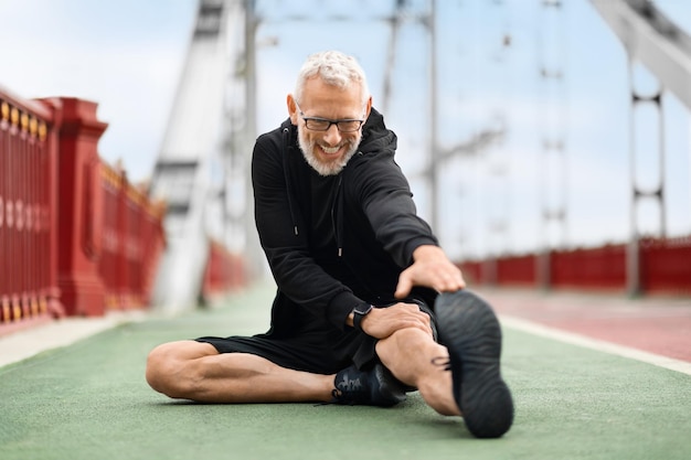 Deportista senior de Wellfit estirando el cuerpo mientras hace ejercicio al aire libre