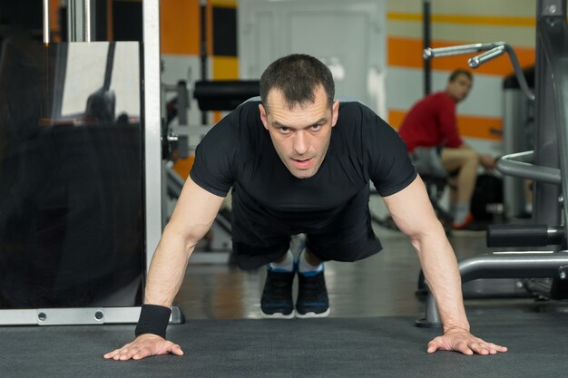 Deportista vistiendo pantalones cortos negros y camiseta haciendo flexiones.