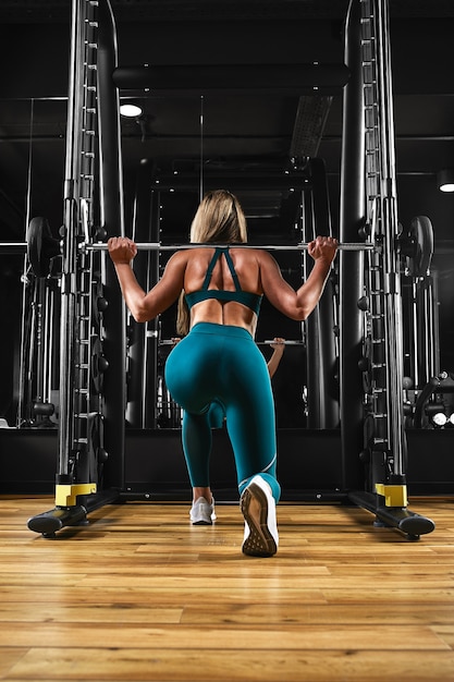 Deportiva chica sexy entrena piernas haciendo ejercicios con pesas en una barra