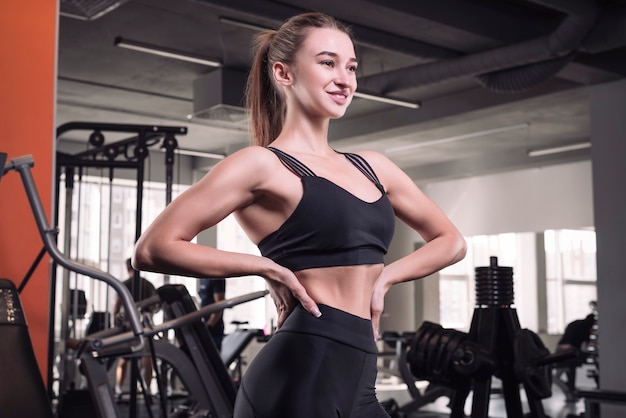 Deportiva joven posando en el gimnasio. Concepto de fitness. Deportes y motivación. Entrenamiento con pesas. Técnica mixta