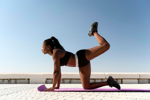 Deportiva mujer fitness multirracial calentando cuerpo musculoso para correr en la playa