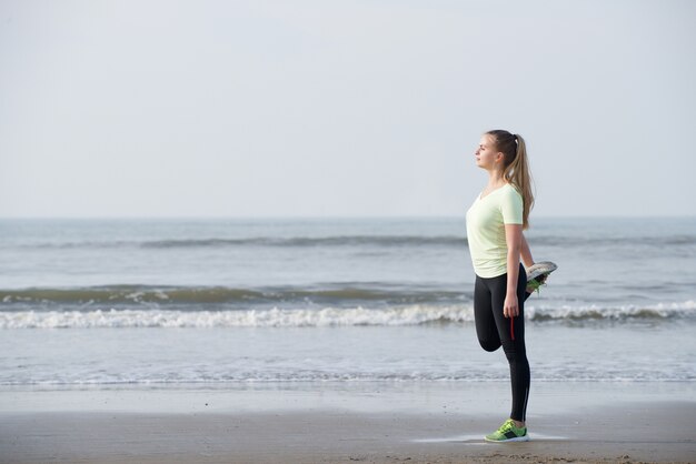 Deportiva mujer joven que estira ejercicio en la playa