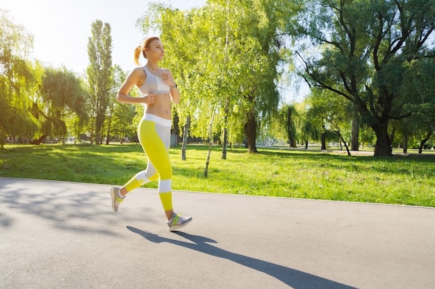 Deportiva mujer joven en ropa deportiva corriendo en el parque por la mañana