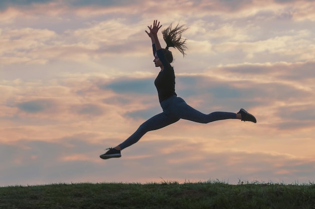 Deportiva mujer joven saltando al aire libre por la mañana las nubes de fondo, la mujer atleta salta hermoso amanecer entrenamiento de la mañana