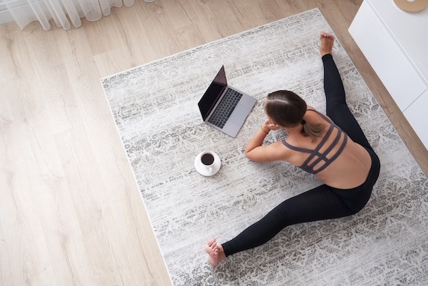 Deportiva mujer joven sentada en el piso en la sala de estar practicar yoga en la lección de computadora en línea femenina