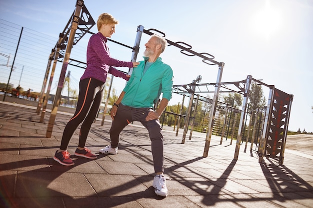 Deportiva mujer madura hablando algo con su marido mientras hace deporte juntos al aire libre feliz