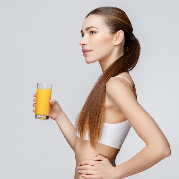 Deportiva mujer sobre fondo gris con vaso de jugo de naranja