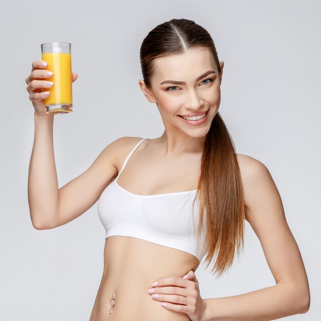 Deportiva mujer sobre fondo gris con vaso de jugo de naranja