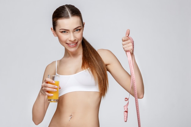 Deportiva mujer sobre fondo gris con vaso de jugo de naranja