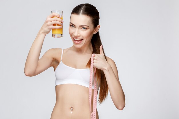 Deportiva mujer sobre fondo gris con vaso de jugo de naranja