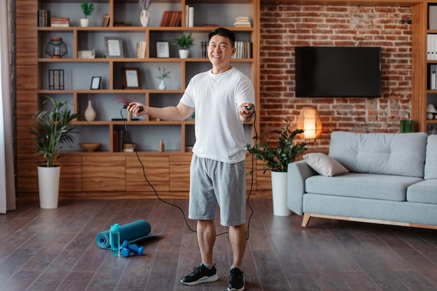 Deportivo hombre de mediana edad con saltar la cuerda haciendo ejercicio en casa haciendo entrenamiento doméstico en la sala de estar de cuerpo entero