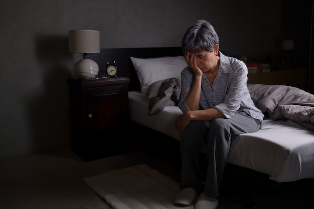 Depressive ältere Frau, die im Bett sitzt, kann nicht vor Schlaflosigkeit schlafen