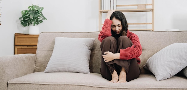 Depressive, einsame, unglückliche, mentale Frau, die allein zu Hause auf dem Sofa sitzt und die Hand im Gesicht hat, fühlt Stress, Traurigkeit und besorgte Enttäuschung, während sie während einer Coronavirus- oder Covid19-Pandemie mit Problemen konfrontiert ist