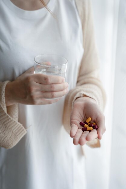 Depressive Frau mit einem Glas Wasser, die unter Kopfschmerzen leidet und Stress mit Antidepressiva in der Nähe bekämpft