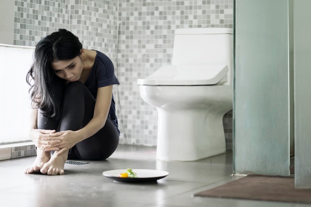 Depressive Frau sitzt mit Salat im Badezimmer