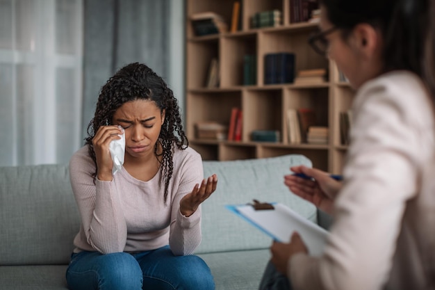 Depressive junge schwarze Dame weint bei Konsultation mit europäischer Ärztin, Psychologin mit