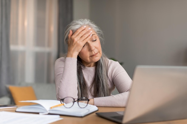 Depressive müde europäische reife frau mit grauem haar leidet unter kopfschmerzen, hat stress und ist unglücklich