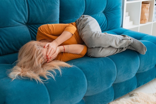 Depressive reife Frau, die mit ihren Armen um sich selbst auf dem Sofa liegt und ihren Kopf mit den Händen bedeckt Unglückliche Frau, die an Schlaflosigkeit leidet, Depressionen, psychologisches Problem