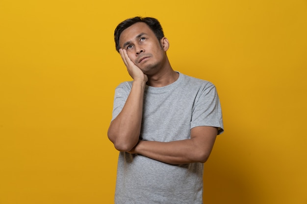 Depressiver asiatischer junger Mann mit dem Gesicht nach unten und versagt. Schuss im Studio lokalisiert auf gelbem Hintergrund.