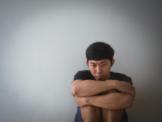 Depressiver asiatischer Mann sitzt an der Wand