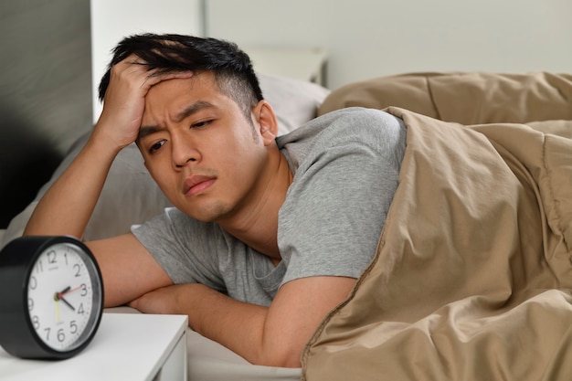 Depressiver junger asiatischer Mann, der im Bett liegt, kann vor Schlaflosigkeit nicht schlafen