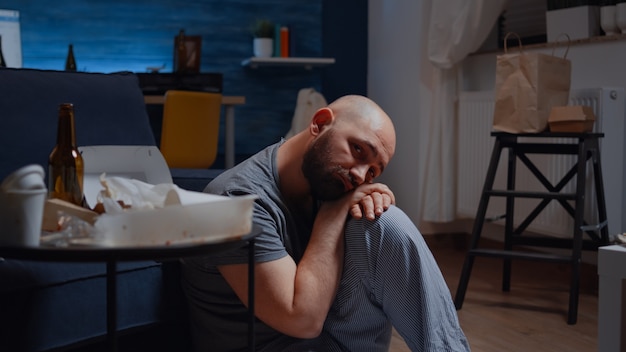 Depressiver mann, der mit enttäuschtem gesichtsausdruck auf dem boden sitzt