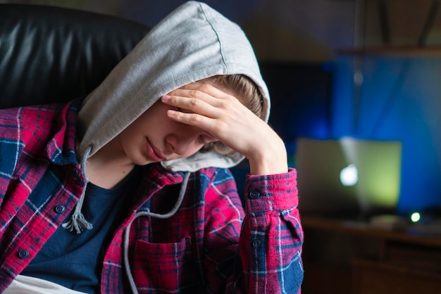 Depressiver Student bedeckt Gesicht mit Handfläche und sitzt nachts auf einem Stuhl b