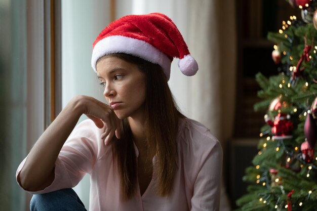 Depressives, einsames Mädchen in rotem Weihnachtsmännchenhut feiert Weihnachten, Neujahr allein, leidet an Stress, Depressionen, schlechter Stimmung, Langeweile, Einsamkeit, Frau, die von den Winterferien enttäuscht ist.