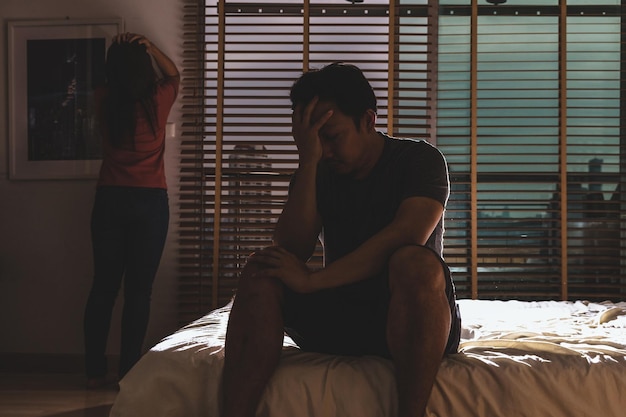 Depressives Paar Mann und Frau sitzen Kopf in Händen auf dem Bett im dunklen Schlafzimmer