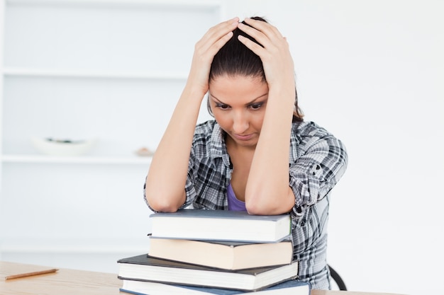 Deprimida joven estudiante apoyándose en libros