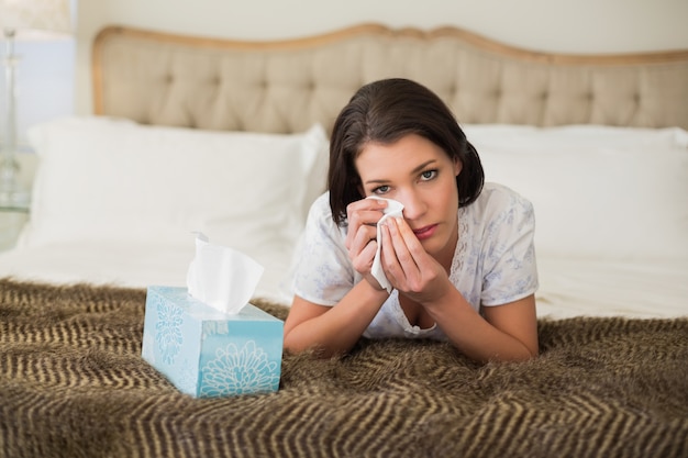 Deprimida mujer de cabello muy castaño limpiándose los ojos con un pañuelo de papel