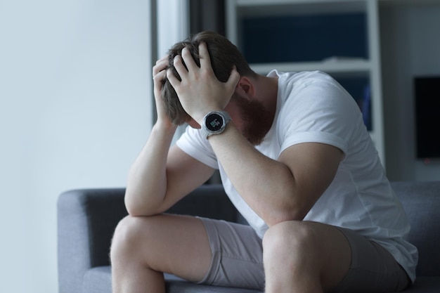 Foto deprimido infeliz hombre triste de mediana edad sentado en el sofá en la sala de estar apoyado en sus manos teniendo