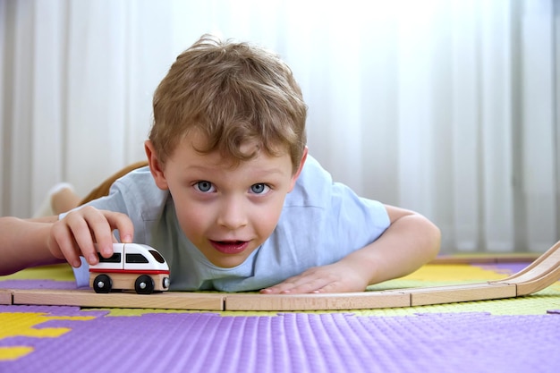 Der 45-jährige Junge schaut in die Kamera und spielt mit einem Zug und einer Holzeisenbahn