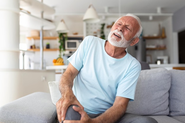Foto der ältere mann sitzt zu hause auf der couch und hat schmerzen im kniegelenk, das sein bein-arthrose-konzept hält