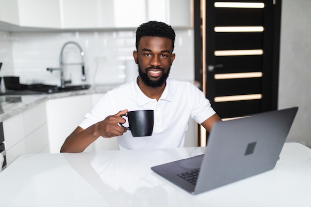 Der afroamerikanische Geschäftsmann trinkt Kaffee, schaut in die Kamera und lächelt, während er in der Küche steht