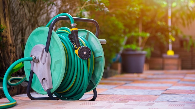 Der alte Wasserschlauch rollt mit Düse auf Fliesenboden im Hausgartenbereich auf