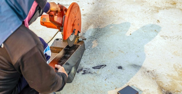 Der Arbeiter in der Arbeit verwendet einen elektrischen Stahlschneider, der große Stahlstangen am Bau schneidet