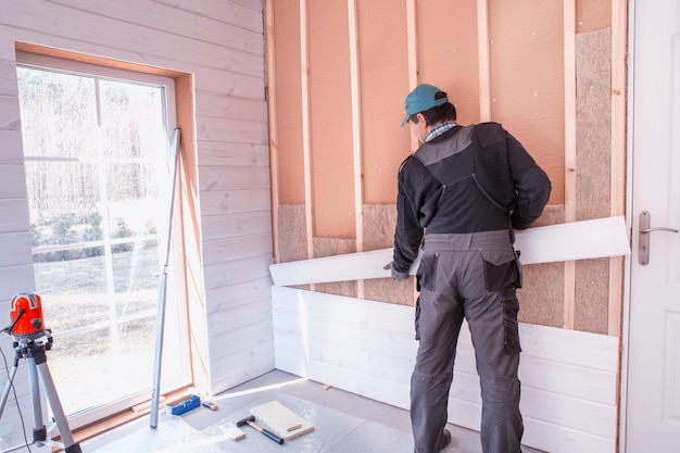 Der Arbeiter macht Abschlussarbeiten an Wänden mit einer weißen Holzplatte mit Laserlinienebene Gebäude wärmeisolierendes Ökoholzrahmenhaus mit Holzfaserplatten